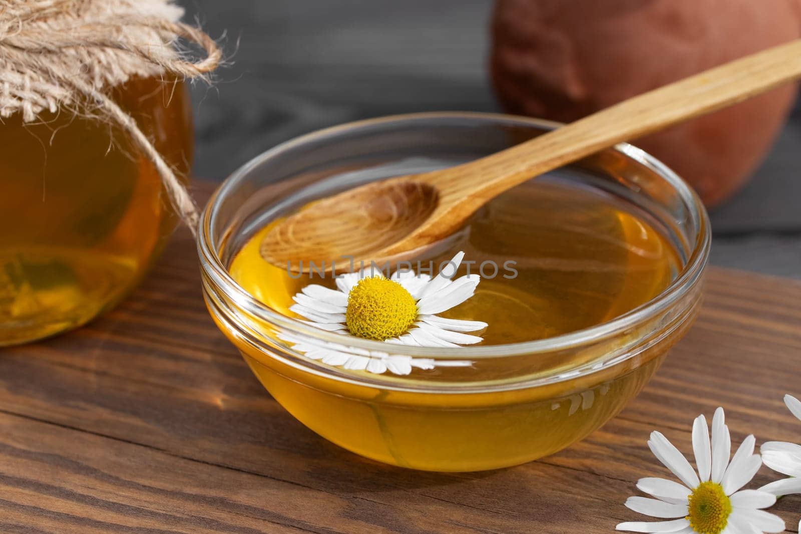 Chamomile syrup in a small bowl and in a jar on a wooden table.