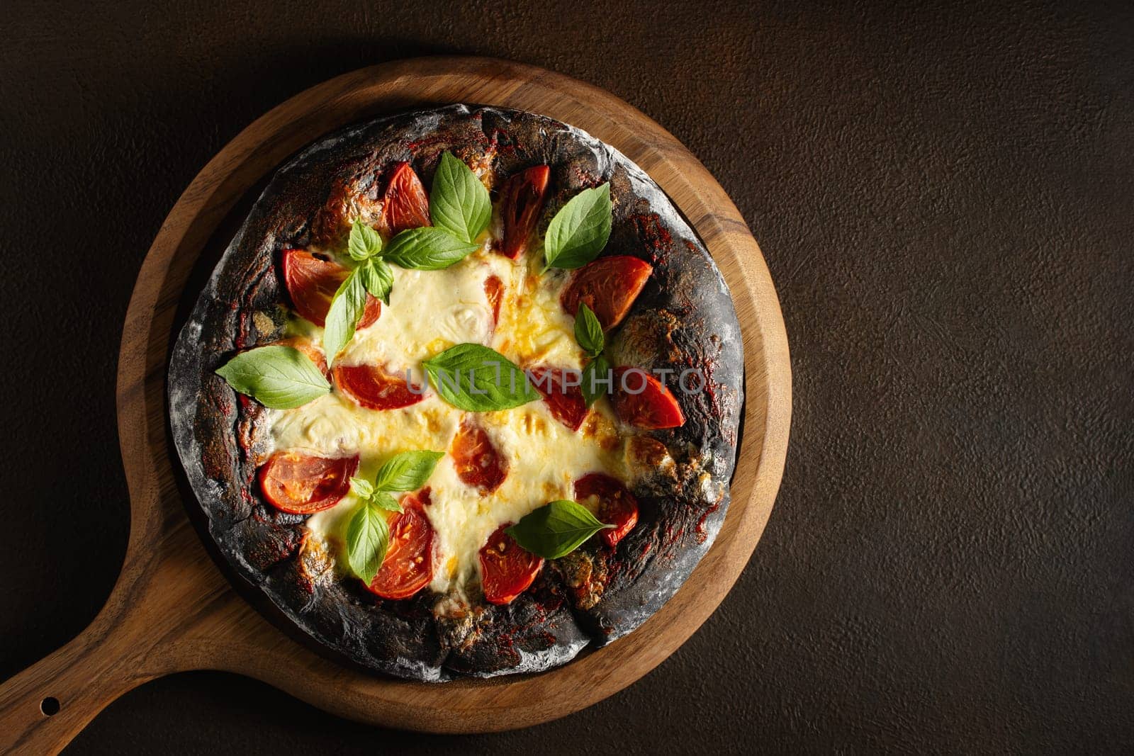 Black pizza margarita with tomatoes, mozzarella and basil. Dough with healthy bamboo charcoal powder, copy space.