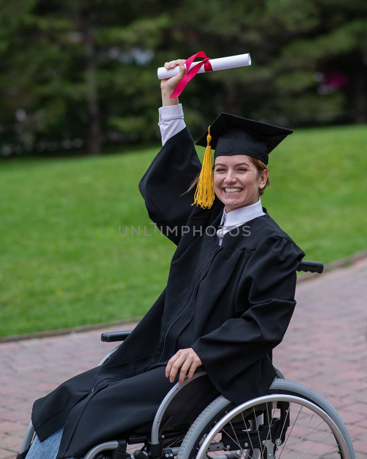 Caucasian woman in a wheelchair in a graduate costume rejoices at receiving a diploma