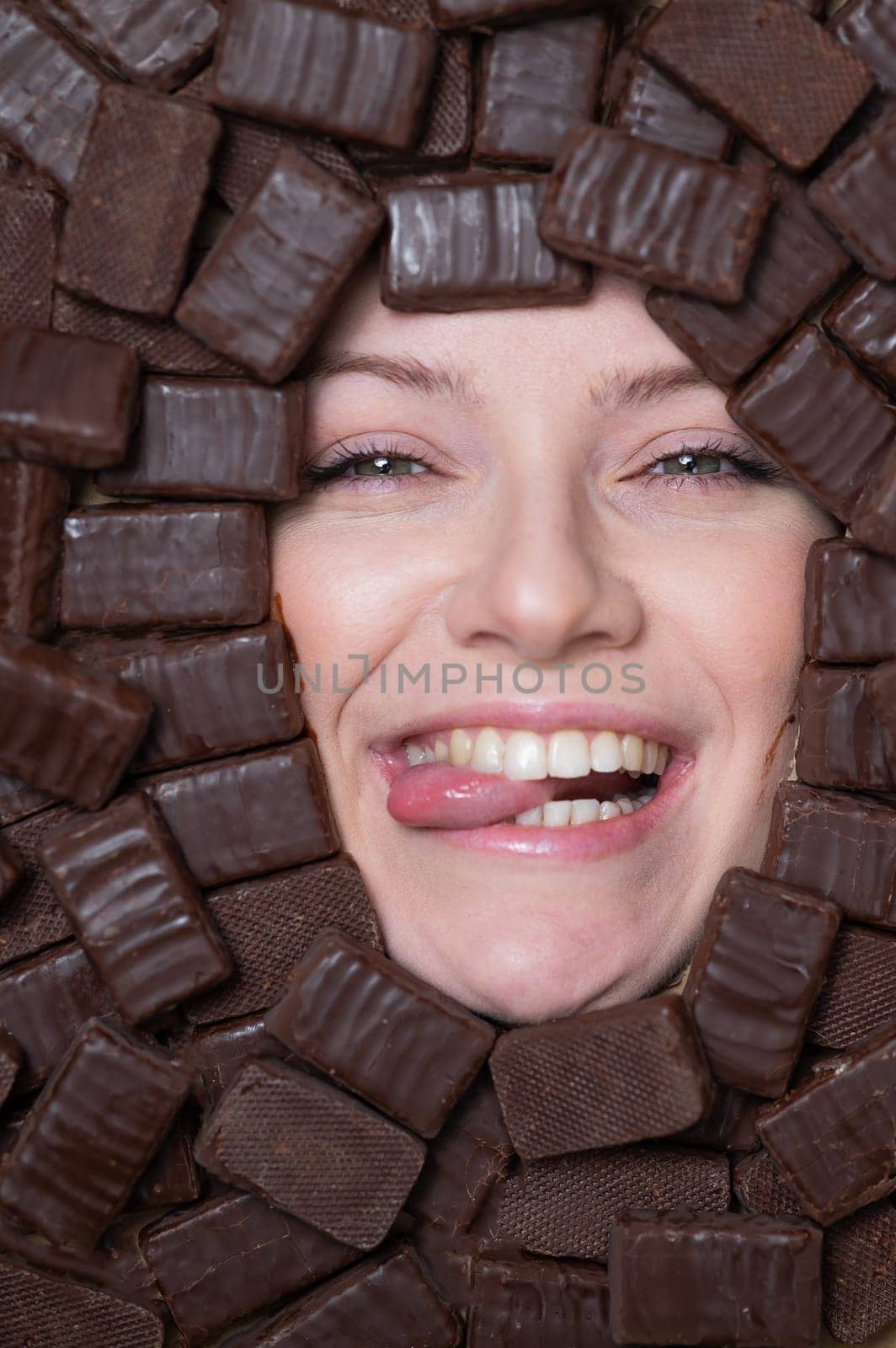 The face of a caucasian woman surrounded by chocolates. girl showing tongue