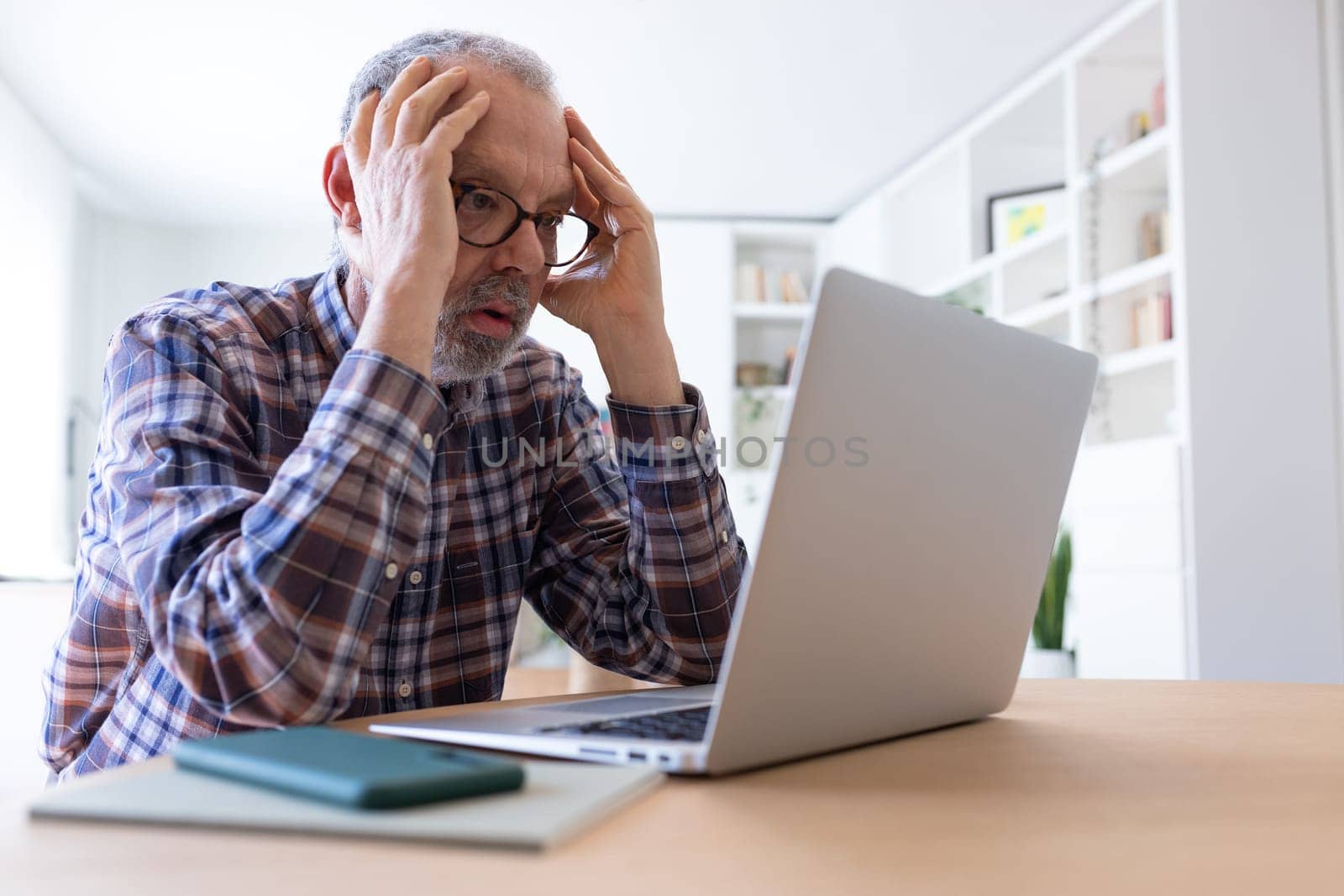 Stressed senior caucasian man working with laptop at home feeling overwhelmed. Technology.