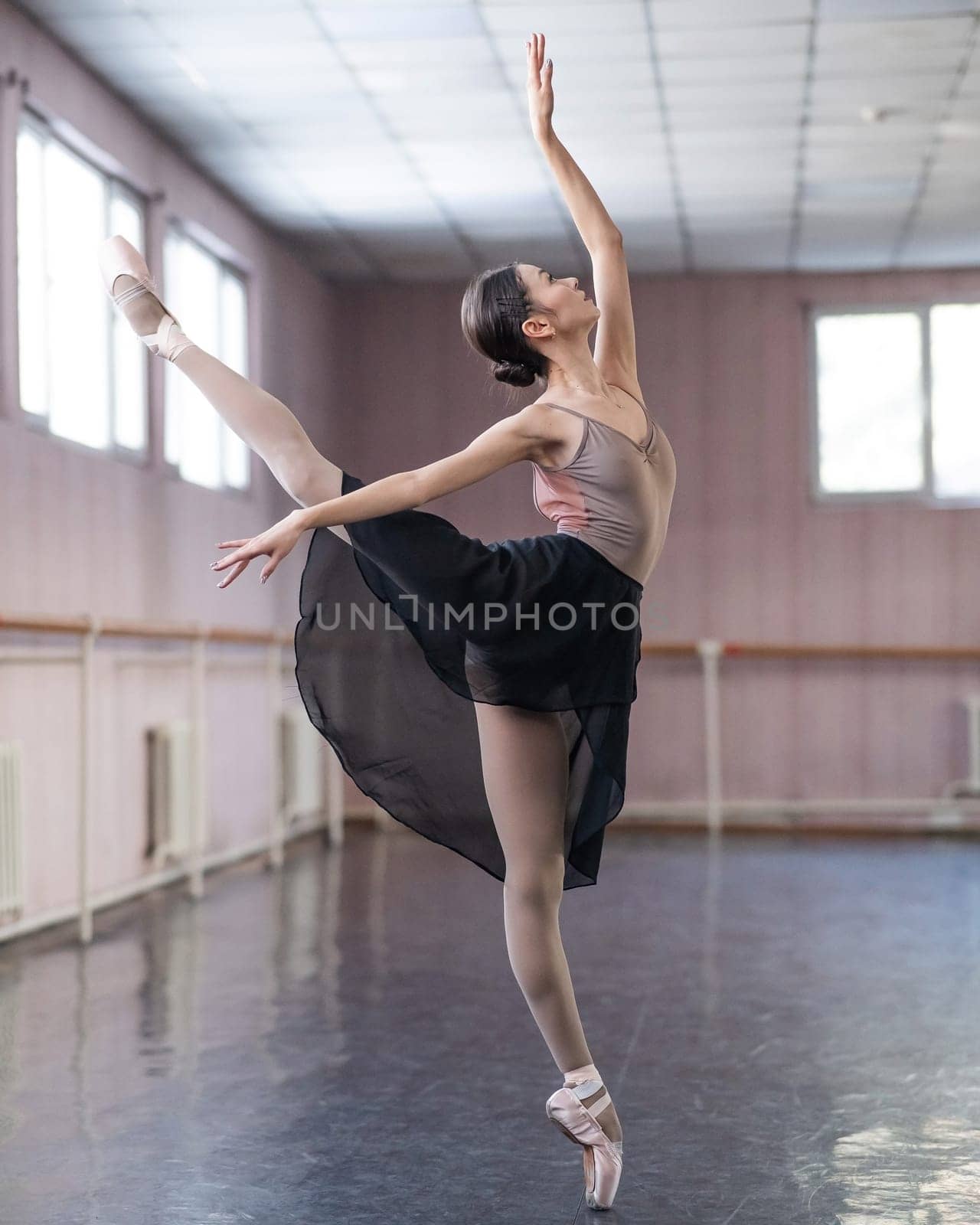 Graceful Asian ballerina in a beige bodysuit and black skirt is rehearsing in a dance class