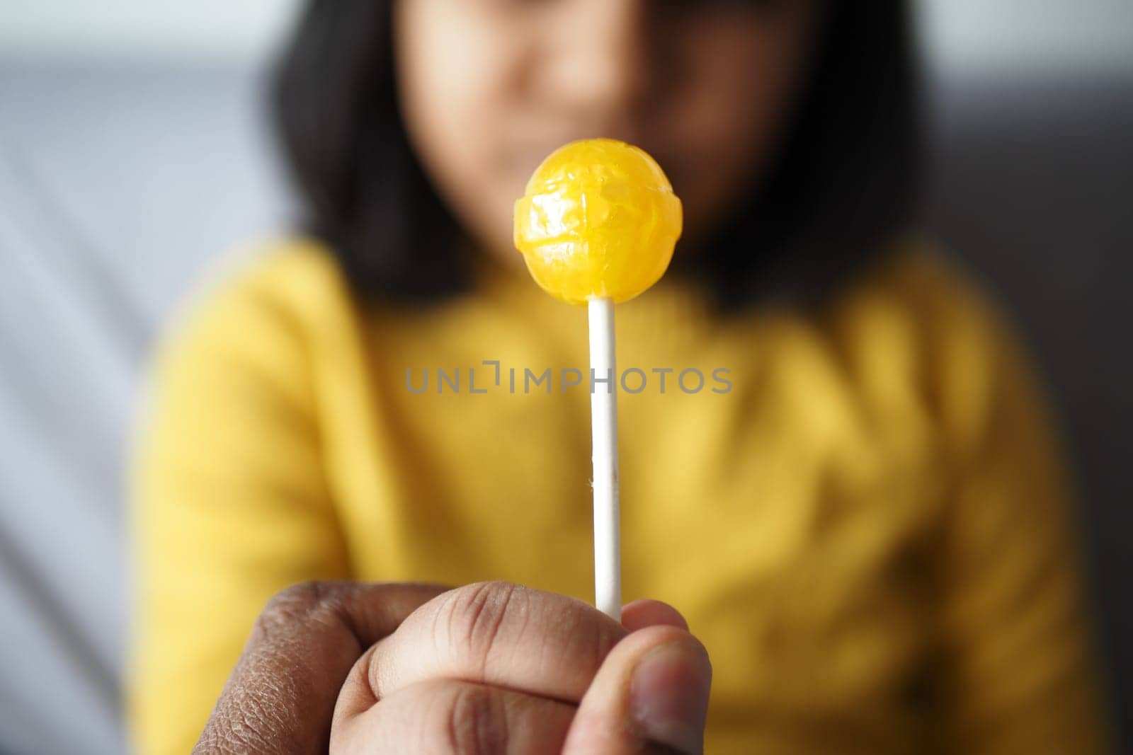 child holding yellow color lollipop candy .