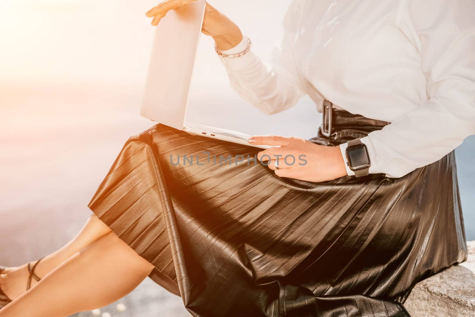 Digital nomad, Business woman working on laptop by the sea. Pretty lady typing on computer by the sea at sunset, makes a business transaction online from a distance. Freelance, remote work on vacation