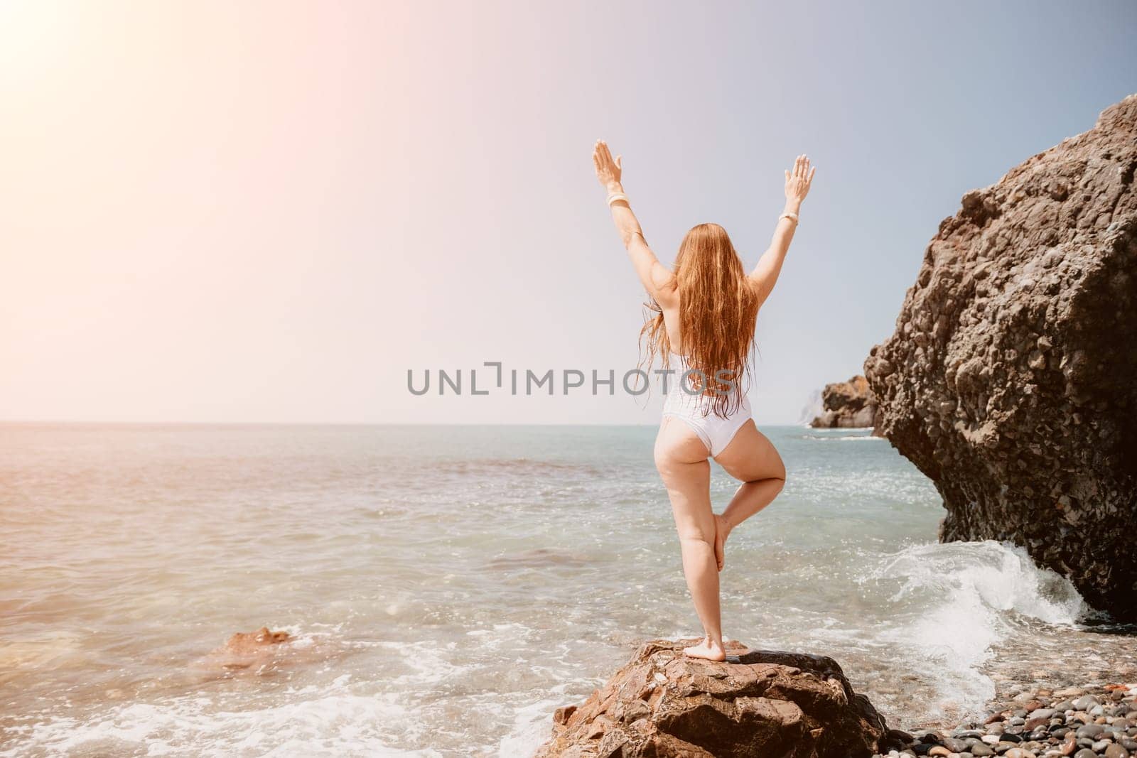 Woman sea yoga. Back view of free calm happy satisfied woman with long hair standing on top rock with yoga position against of sky by the sea. Healthy lifestyle outdoors in nature, fitness concept