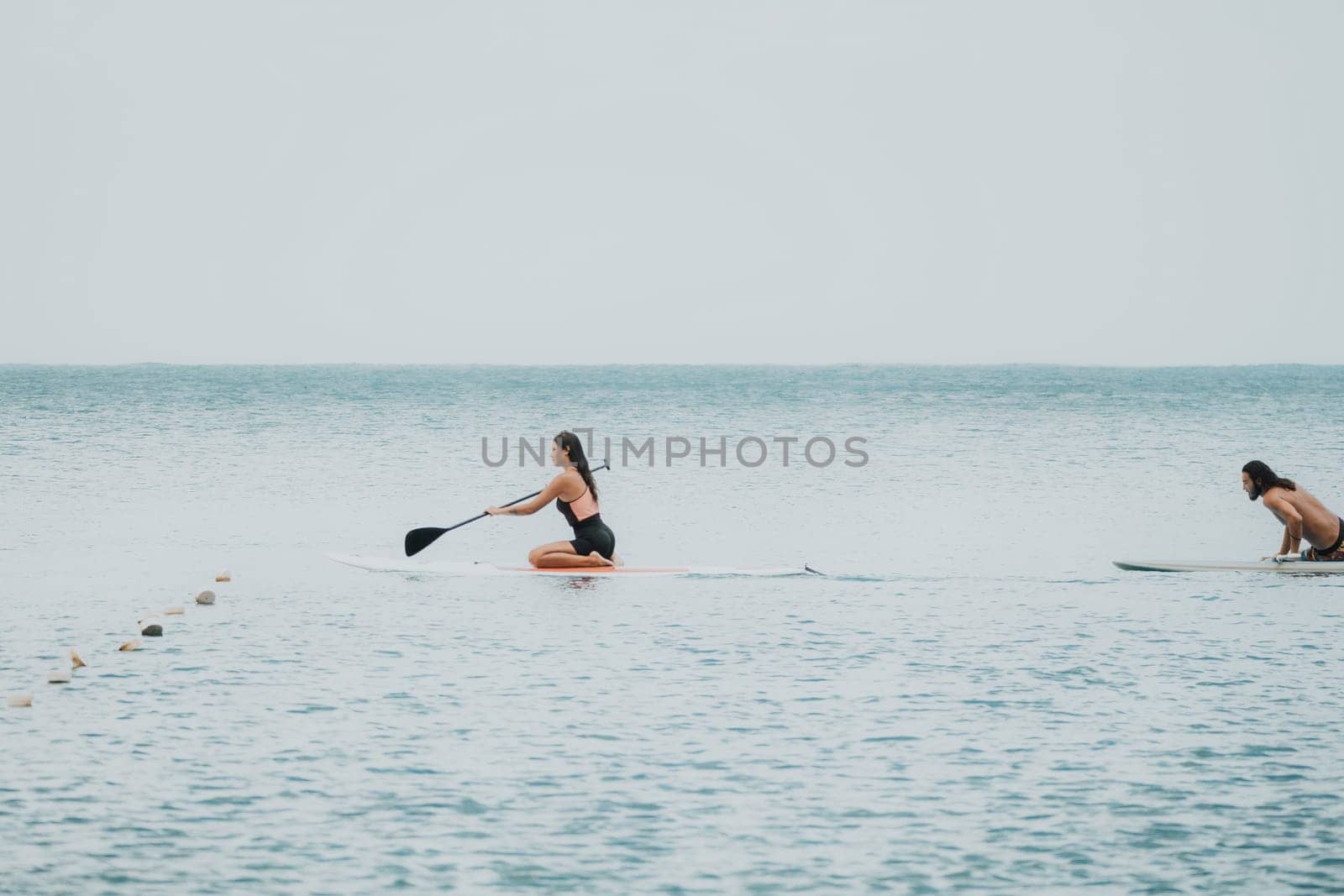 Sea woman and man on sup. Silhouette of happy young woman and man, surfing on SUP board, confident paddling through water surface. Idyllic sunset. Active lifestyle at sea or river