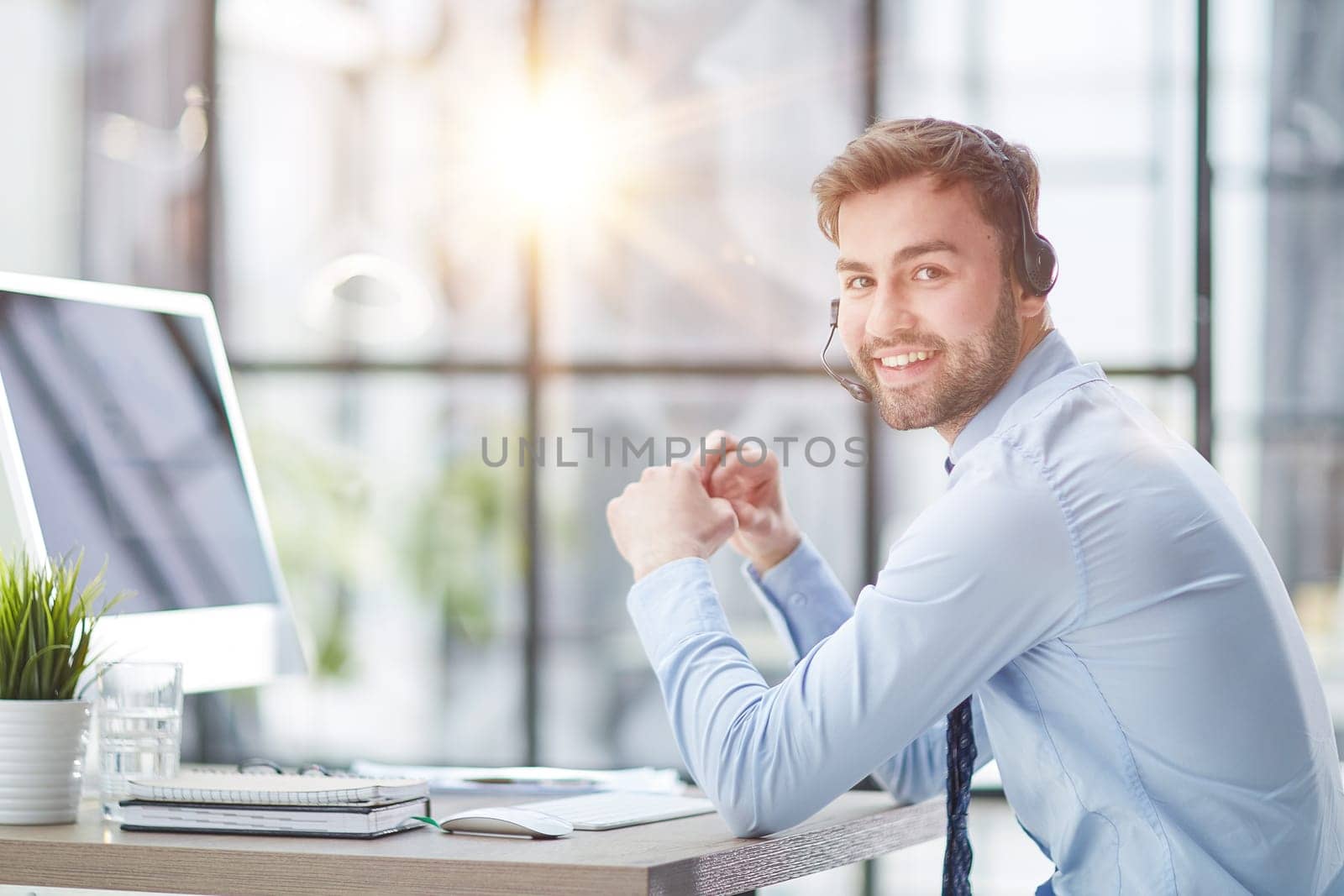 Young handsome male customer support phone operator with headset working in his office