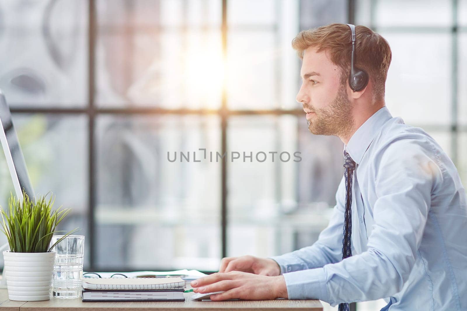 Young handsome male customer support phone operator with headset working in his office