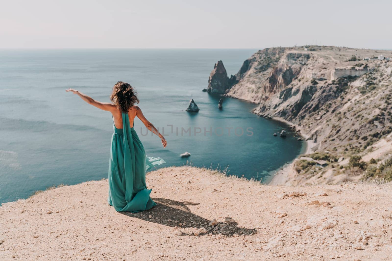 Woman green dress sea. Female dancer posing on a rocky outcrop high above the sea. Girl on the nature on blue sky background. Fashion photo