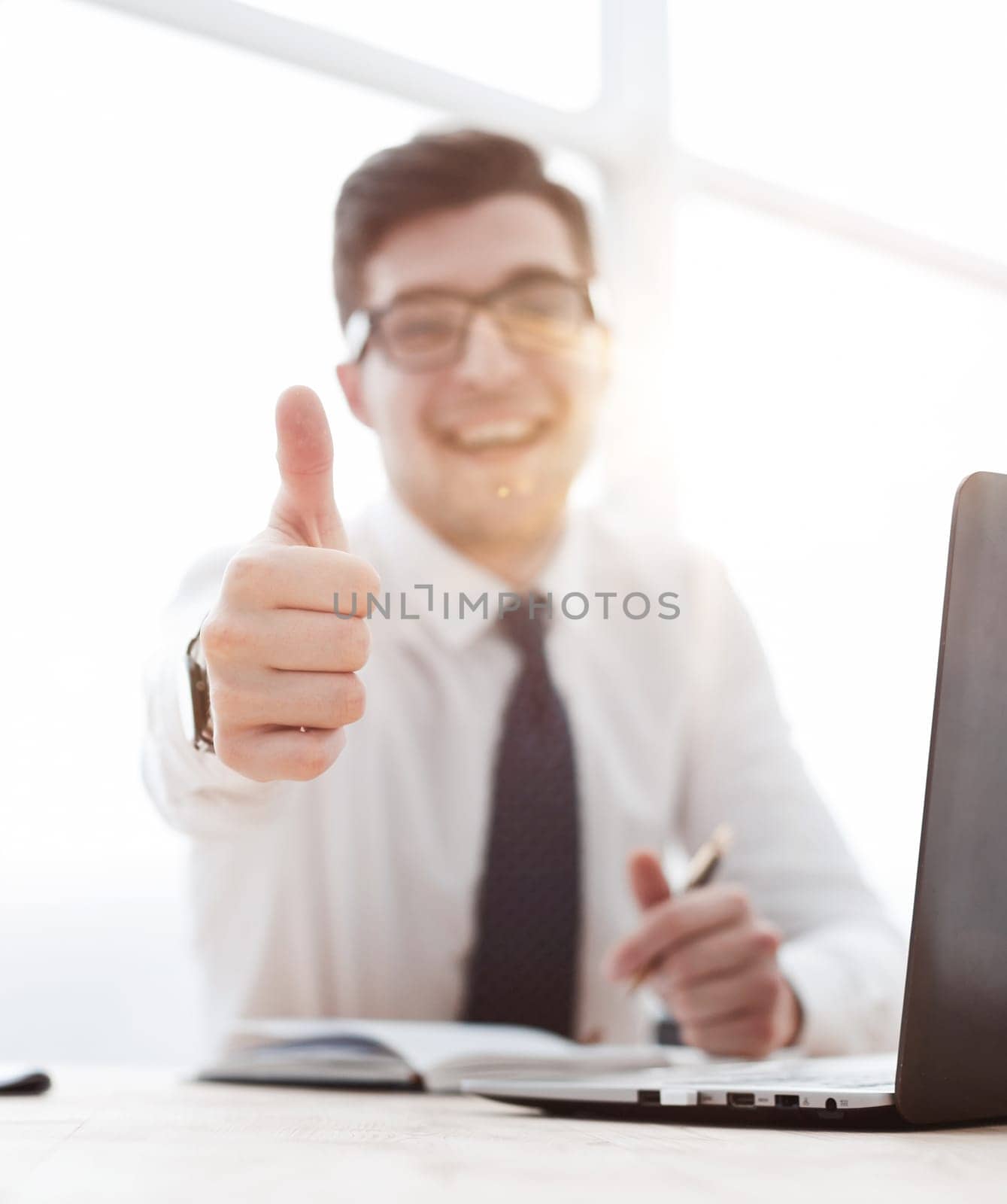 Cheerful young businessman standing and showing thumbs up in office