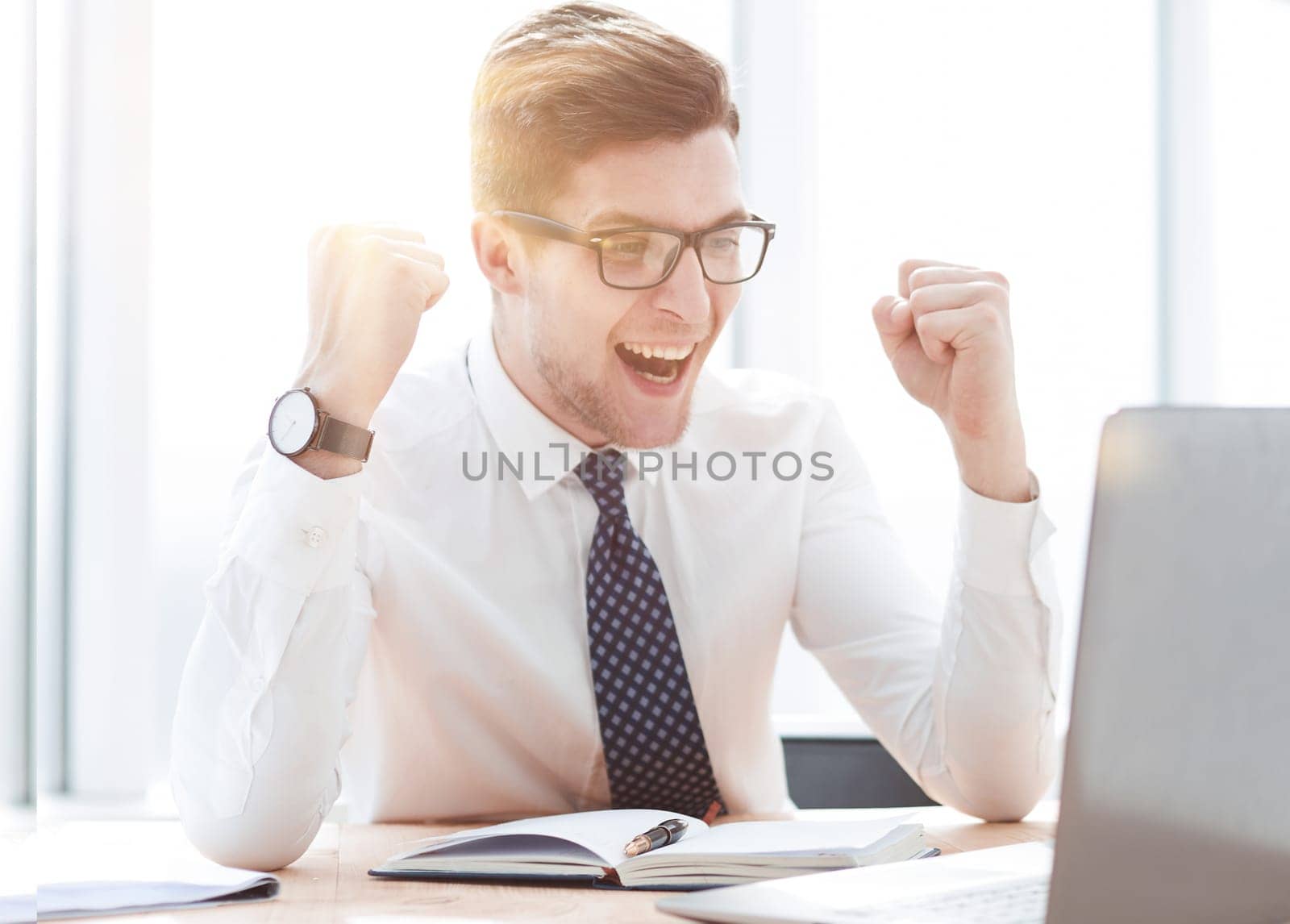 Happy young businessman raising hands in front of laptop