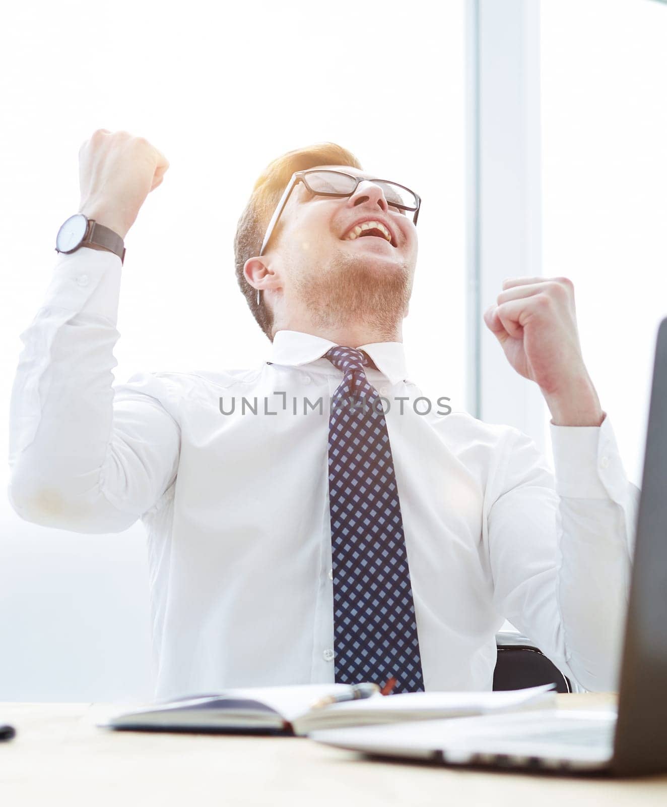 Happy young businessman raising hands in front of laptop