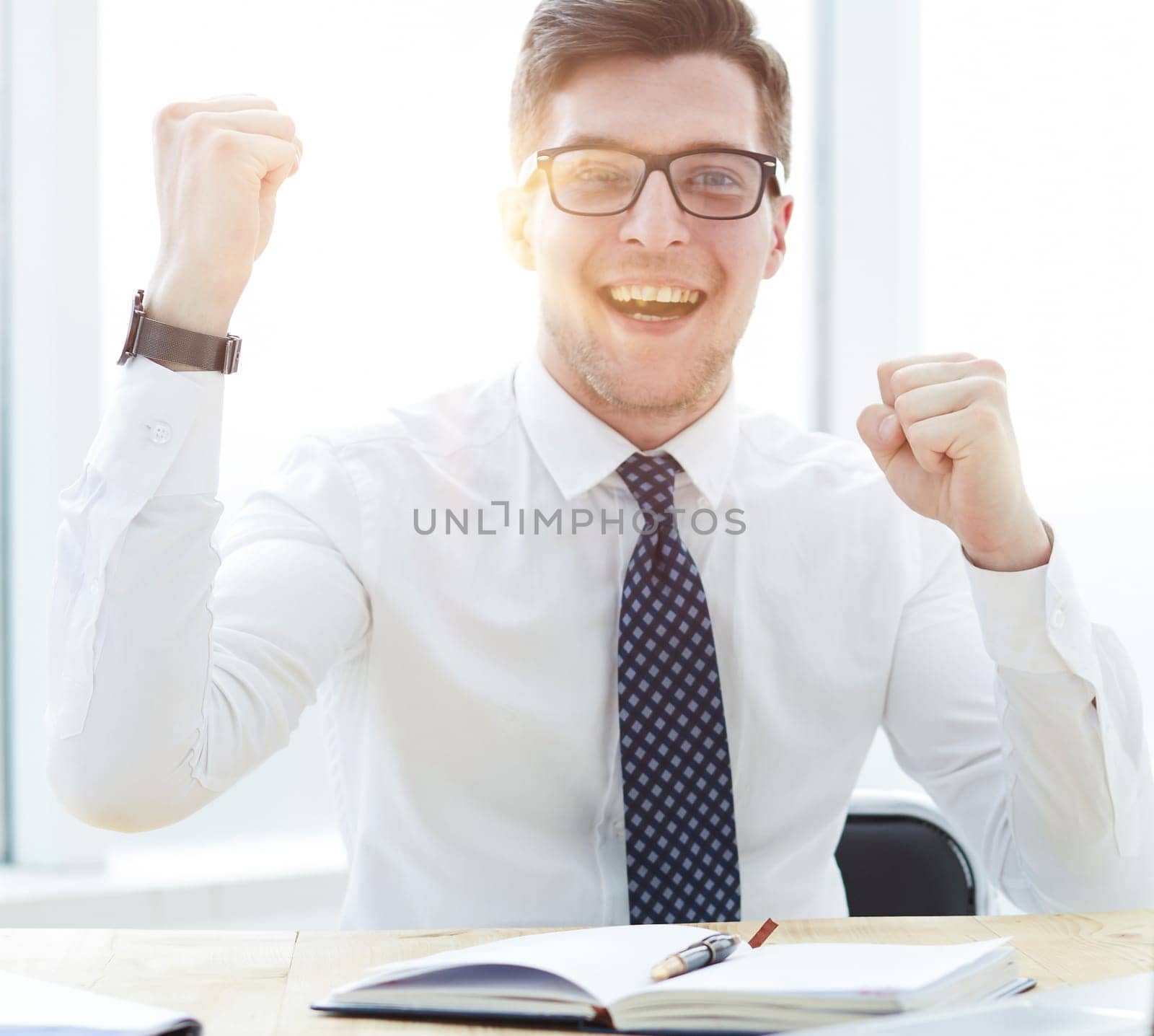 Happy young businessman raising hands in front of laptop