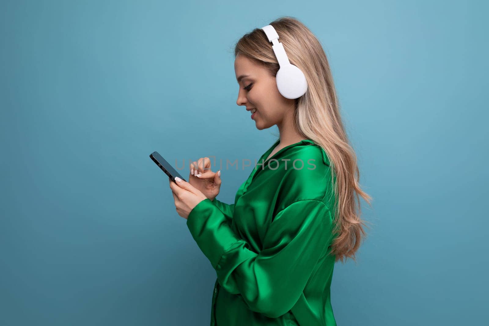Profile photo of an attractive blond young adult woman in headphones on a blue background.