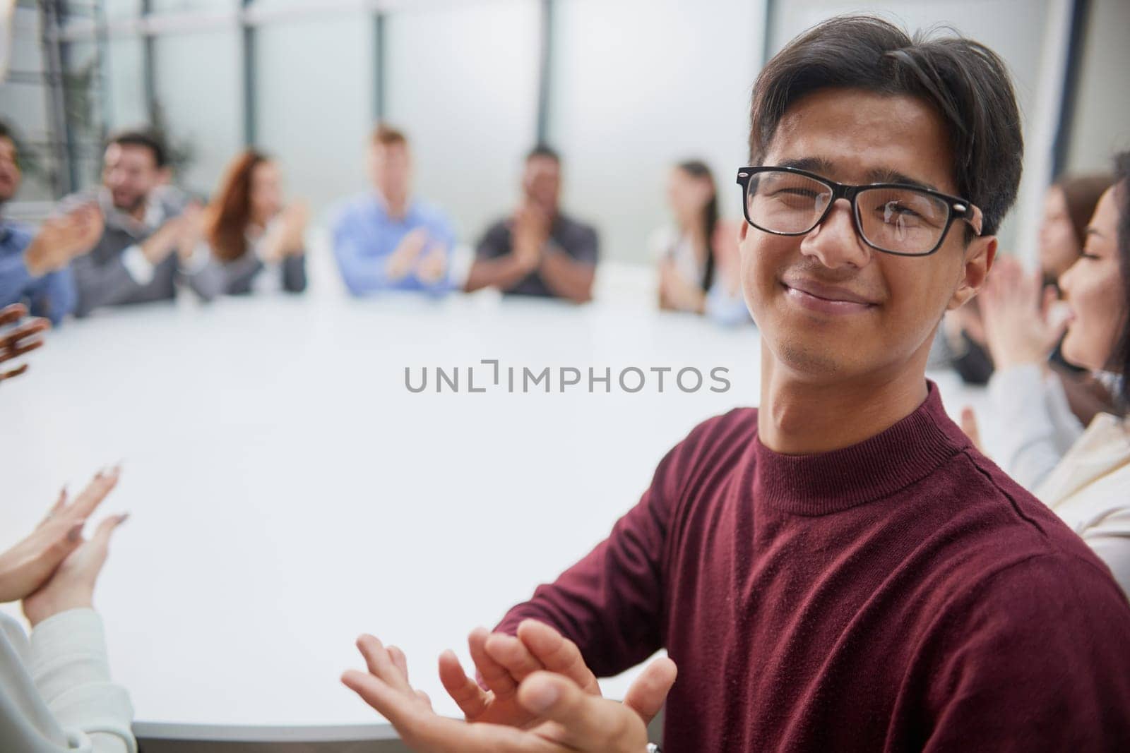 Young handsome businessman in glasses posing for the camera against the background of his colleagues