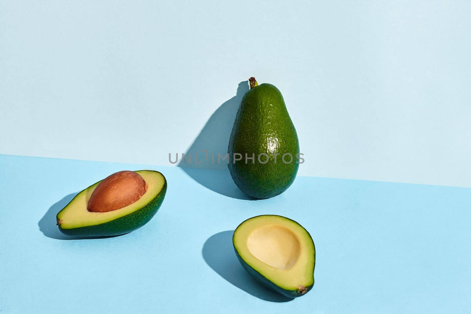 Composition of fresh fruits, whole avocado and two halfs of cutted avocado on blue background. Mock up, two-colored pastel