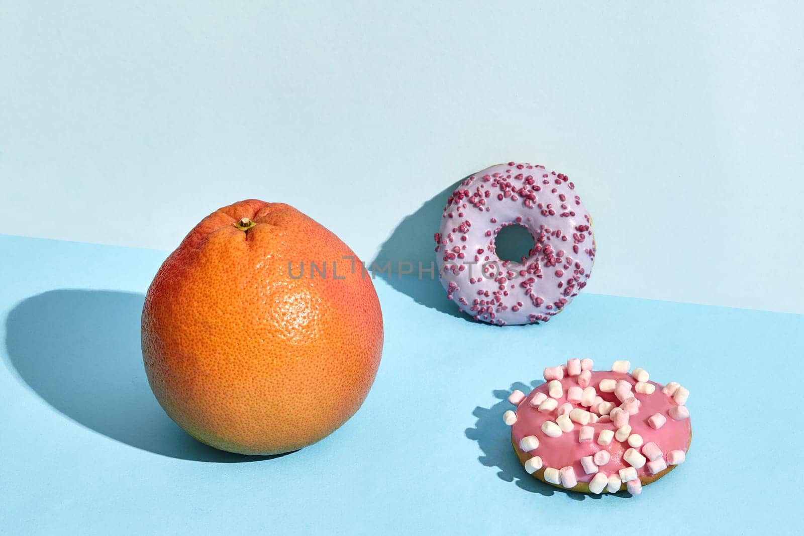 Composition of fresh fruits and sweets, two donuts and juicy grapefruit on blue background. Mock up, two-colored pastel