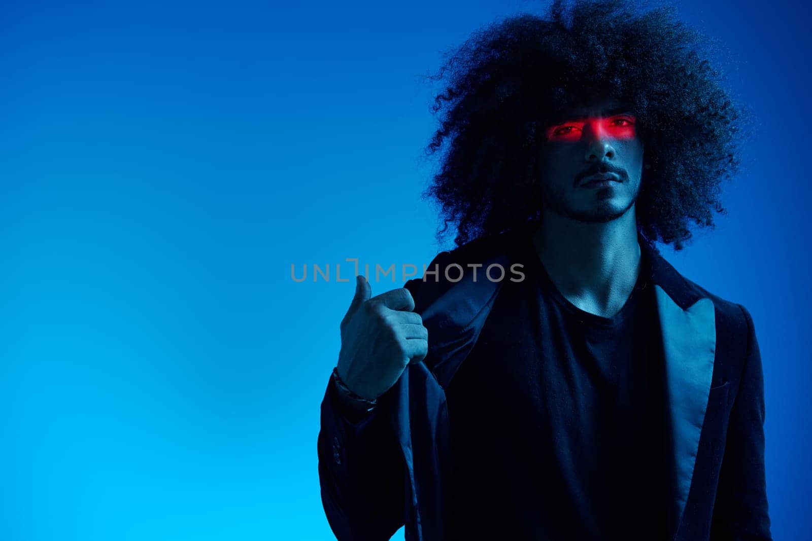 Fashion portrait of a man with curly hair on a blue background with a red stripe of light, multicolored light, trendy, modern concept. by SHOTPRIME
