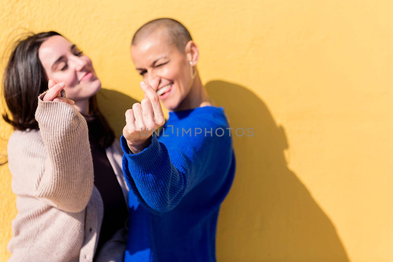 two young caucasian fiends making heart shape with fingers with a yellow background, focus on the hand, copy space for text