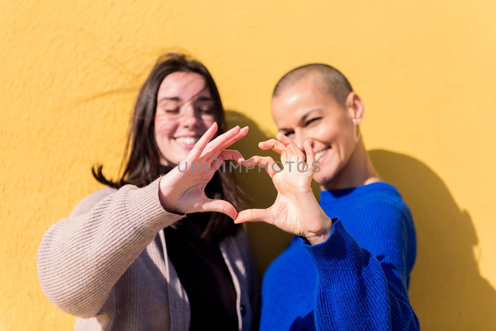 two young caucasian fiends making heart shape with hands with a yellow background, focus on the hand, copy space for text