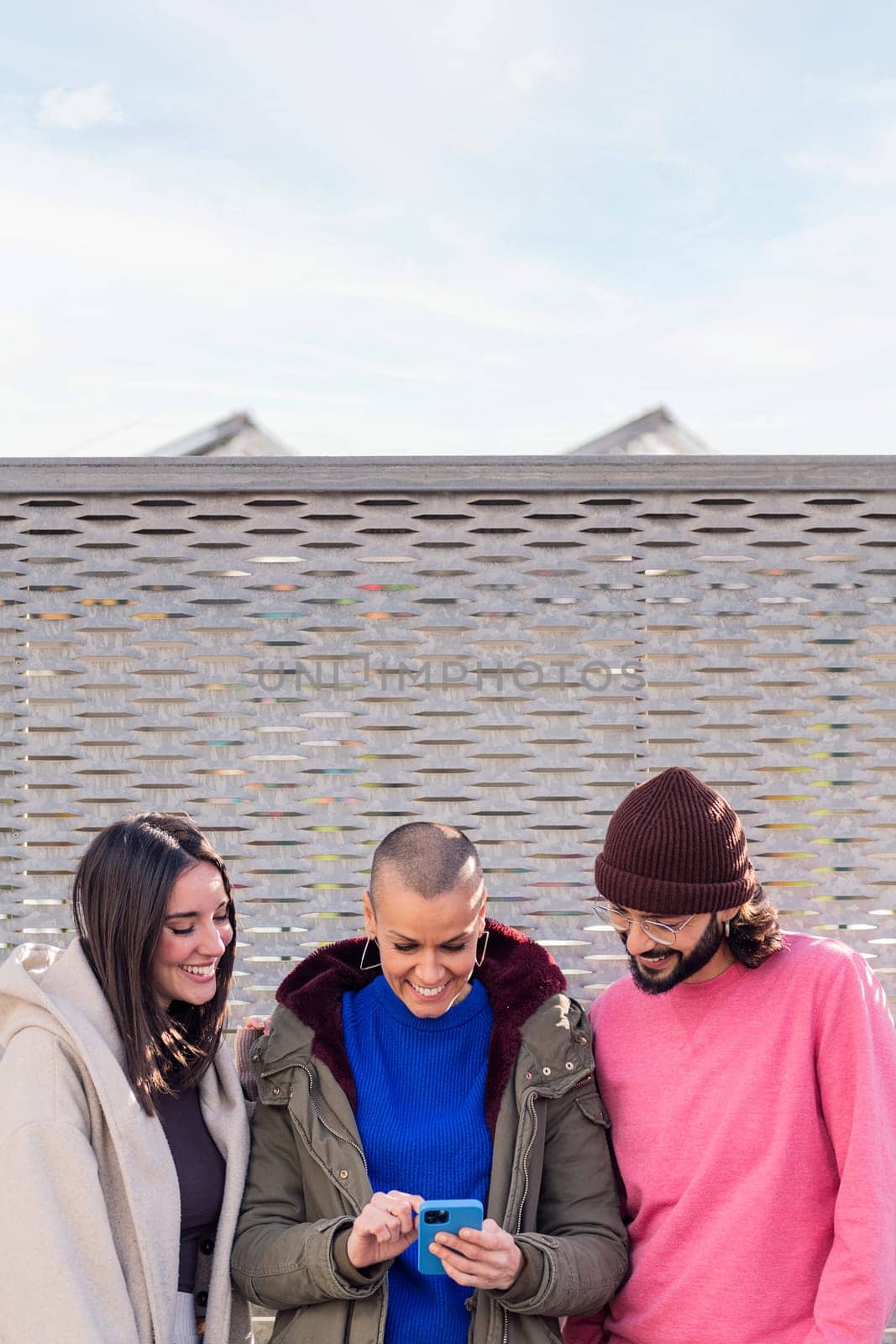 three young friends smiling happy and enjoying the moment using together a mobile phone, concept of technology of communication and modern lifestyle, copy space for text