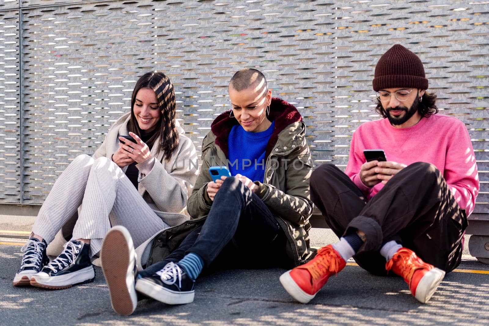 three young friends sitting in the floor scrolling together through social media with mobile phone, concept of friendship and modern lifestyle