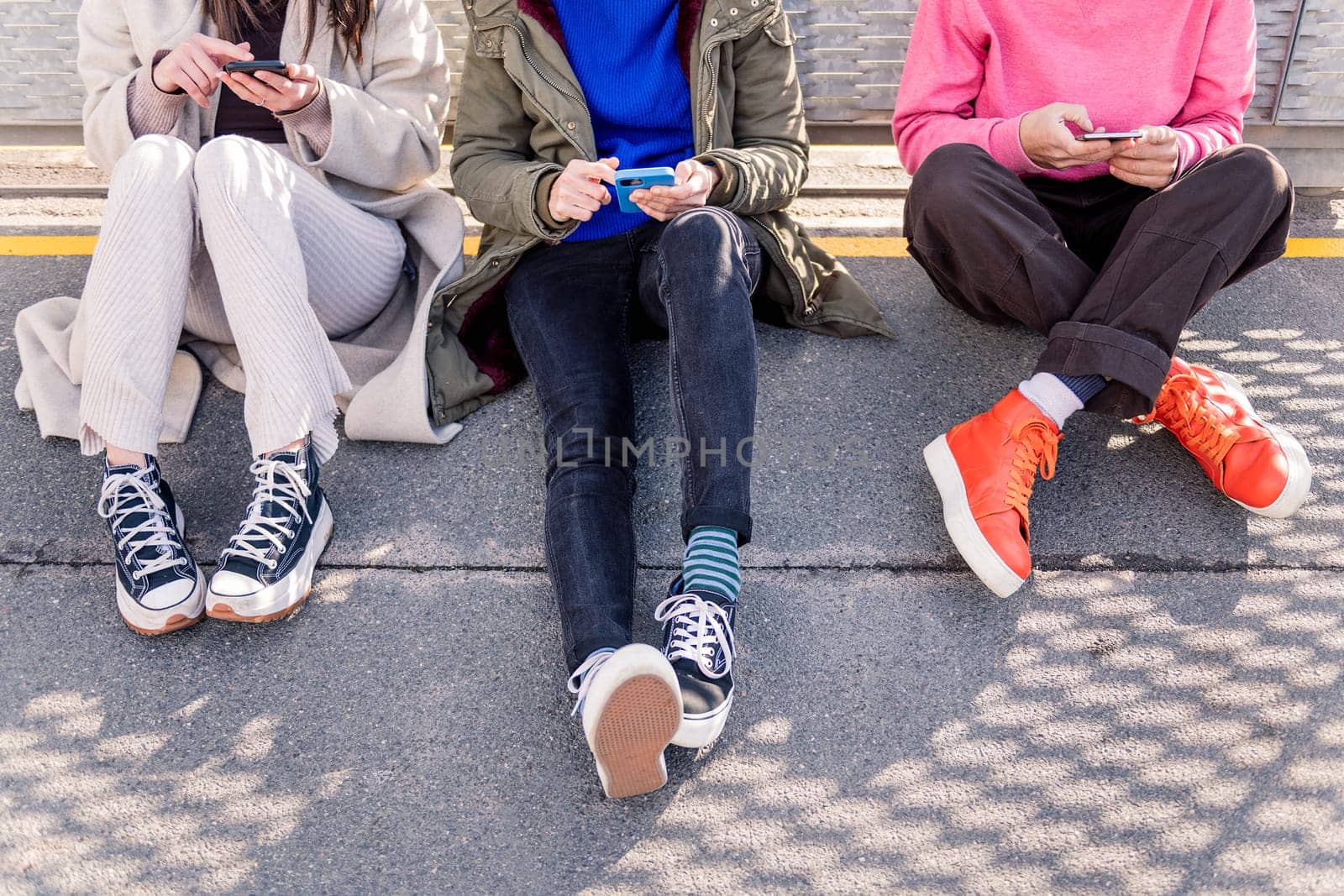 three unrecognizable friends sitting in the floor scrolling together through social media with mobile phone, concept of friendship and modern lifestyle