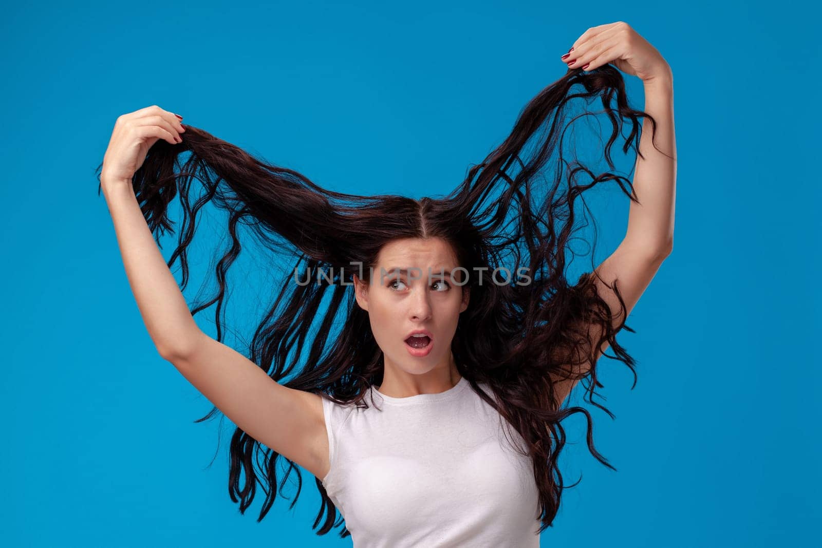 Surprised woman is pulling her hair and looking away on the blue background