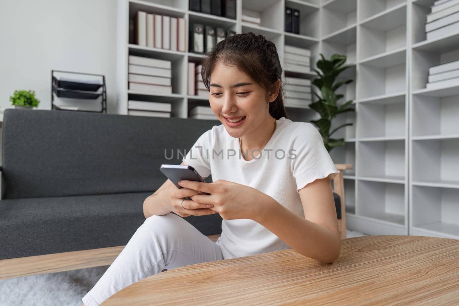 Happy young asian woman using mobile phone while sitting a couch at home.