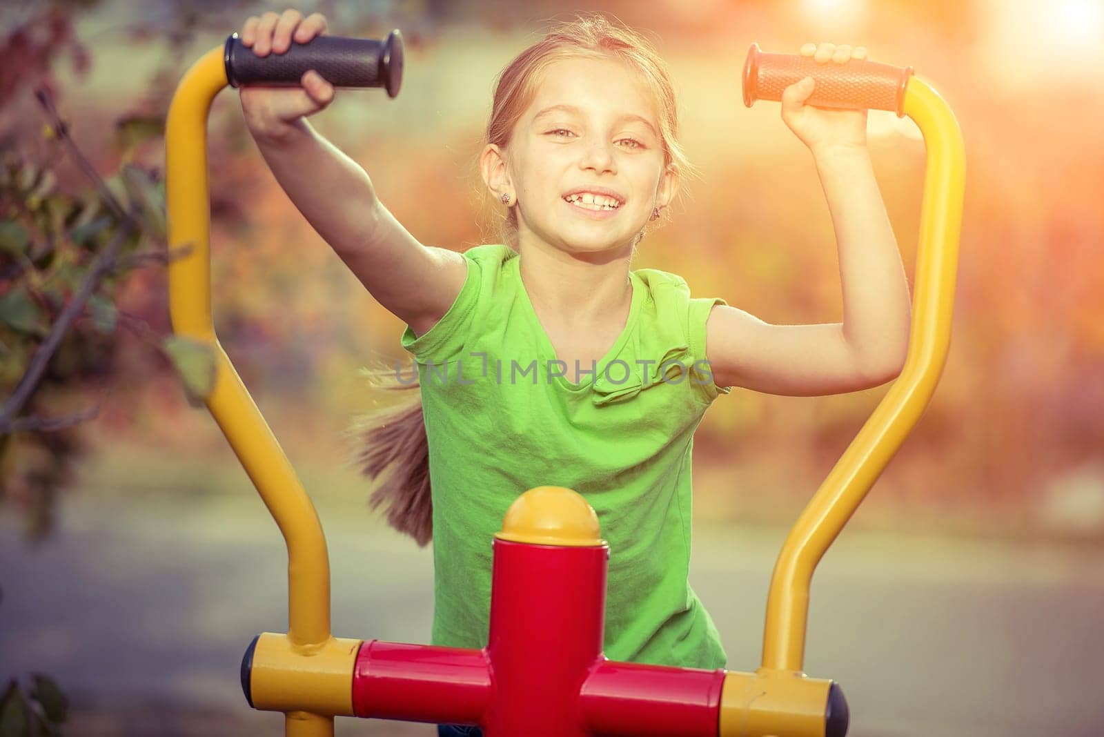 Little girl does exercises at simulator in park