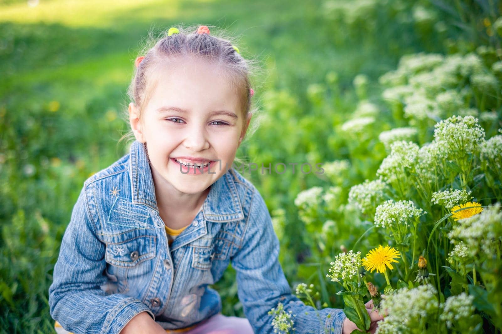 Smiling attractive girl sitting near grass and flowers in jeans jacket