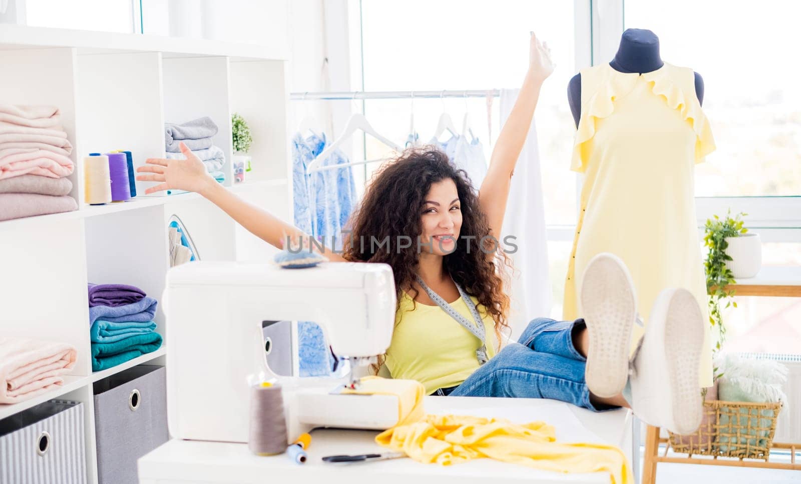 Excited designer sitting with raised hands in sewing atelier