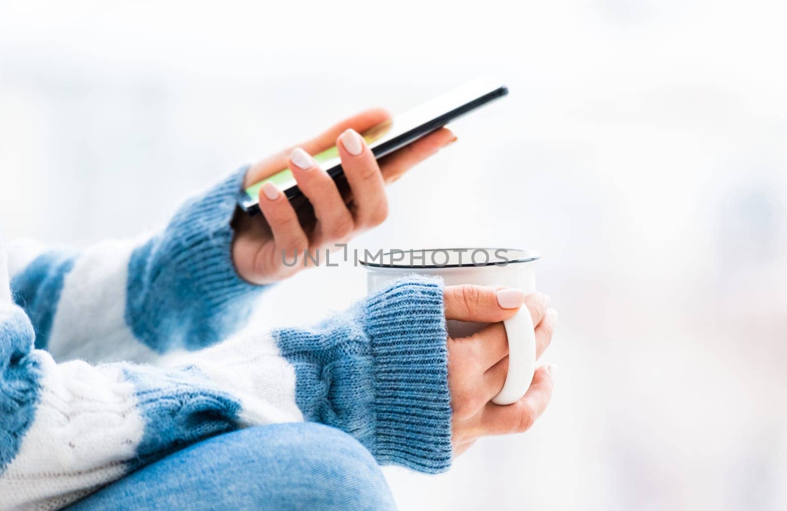 Cup and smartphone in female hands close up