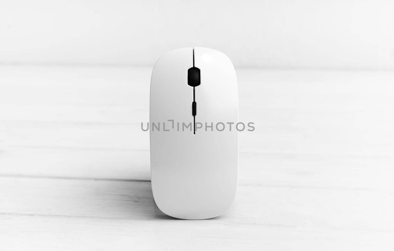 Wireless computer mouse standing vertically on white wooden table