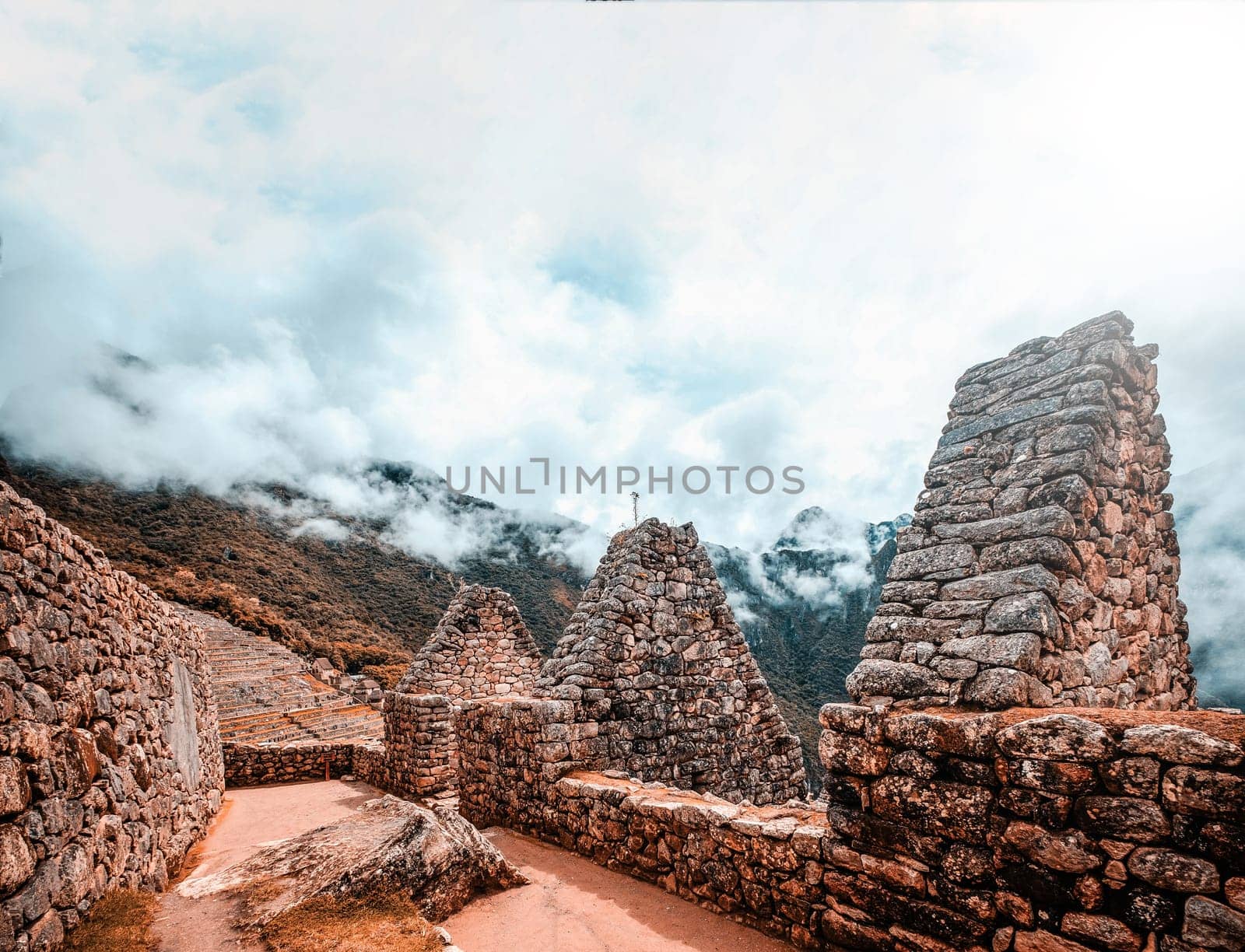 Sunshine breathtaking view of Machu Picchu stone anchient walls and temple among mountains covered with clouds