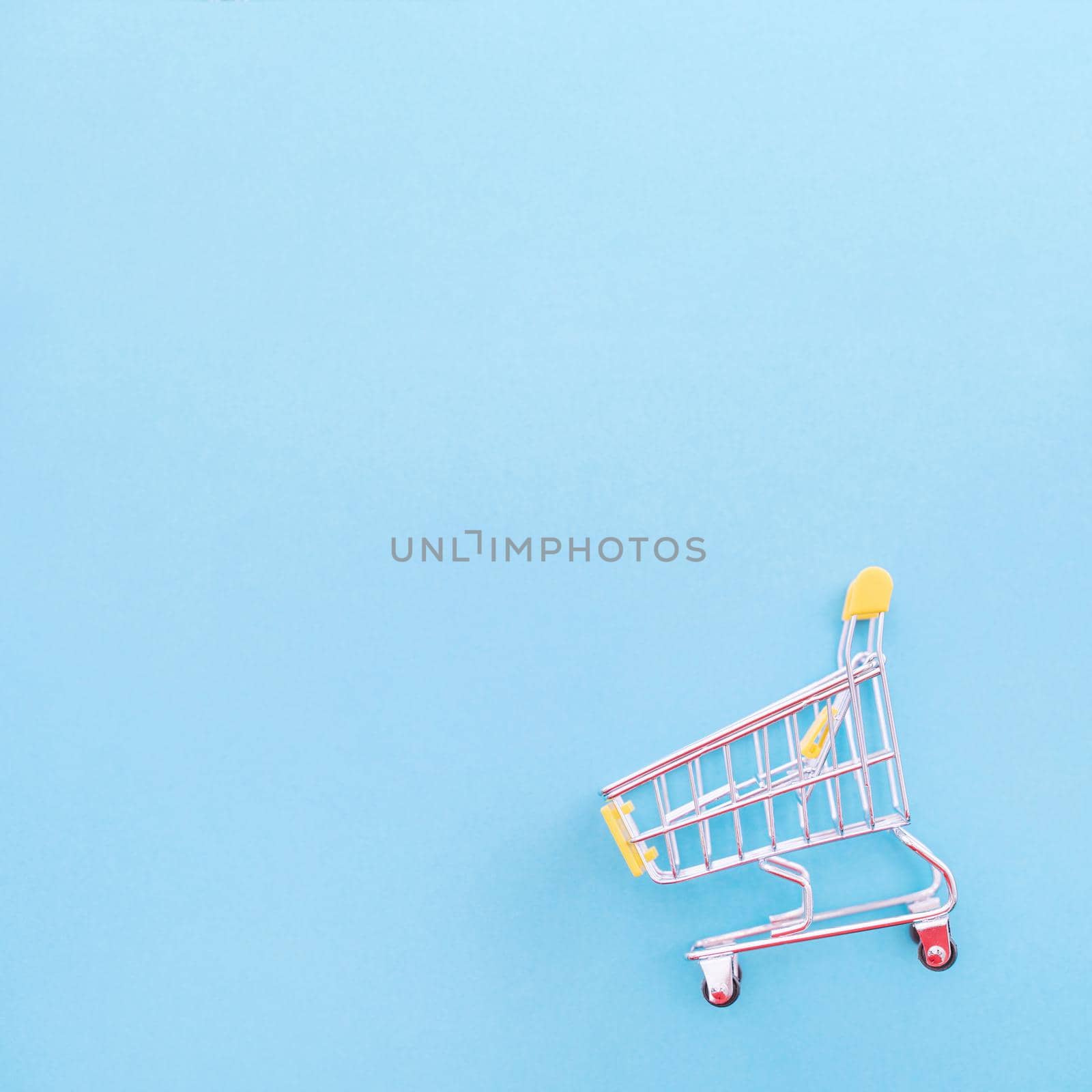 Abstract design element, annual sale, shopping season concept, mini yellow cart with colorful paper bag on pastel blue background, top view, flat lay