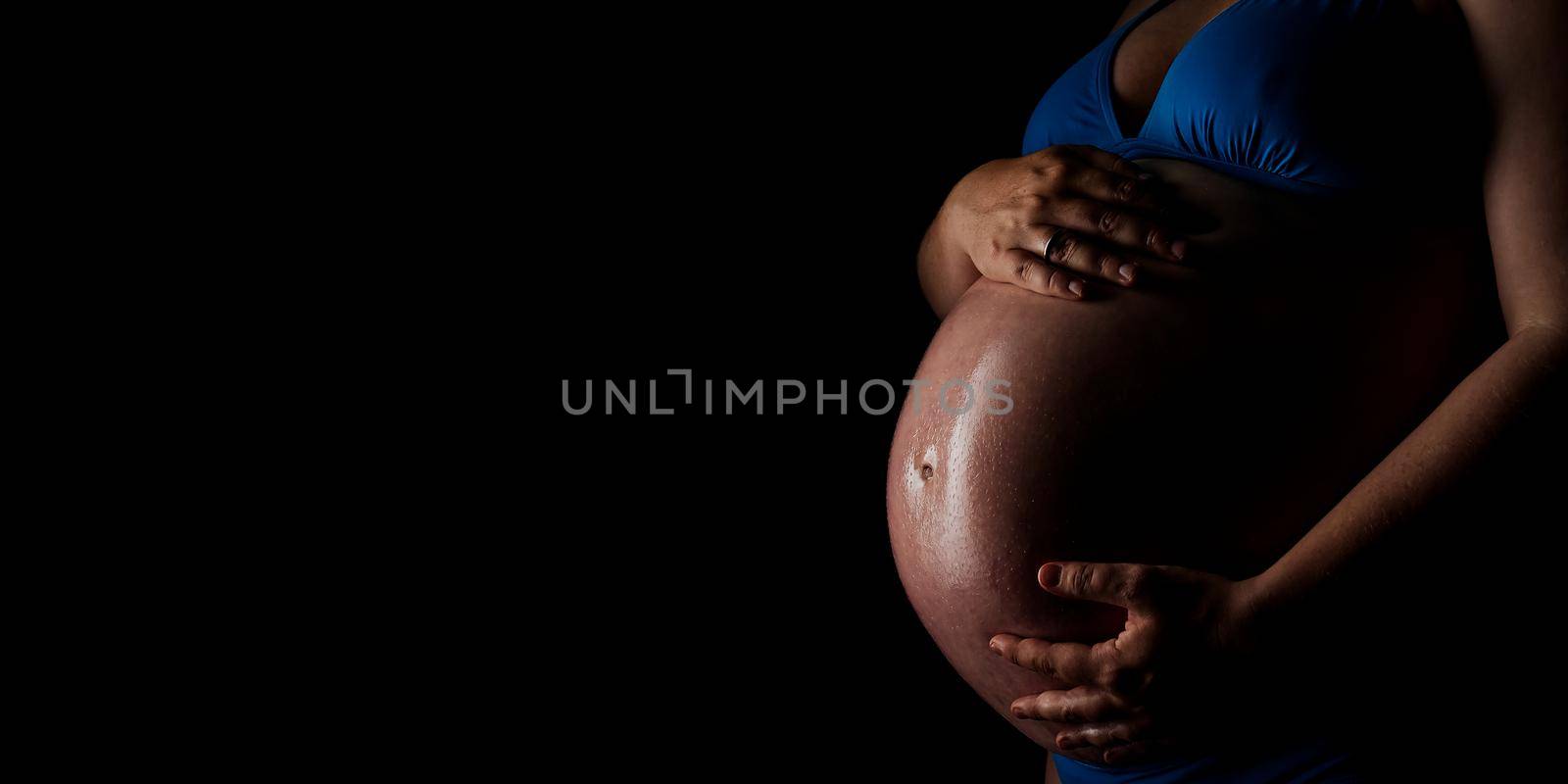 Belly of a pregnant woman on the black background. Belly of a pregnant woman in low key. Body of a 9-month pregnant woman. 40 weeks pregnant women infront of black backdrop