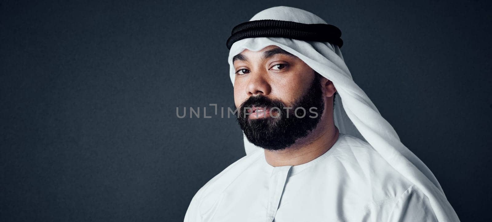 He loves the traditional look. Studio shot of a young man dressed in Islamic traditional clothing posing against a dark background. by YuriArcurs