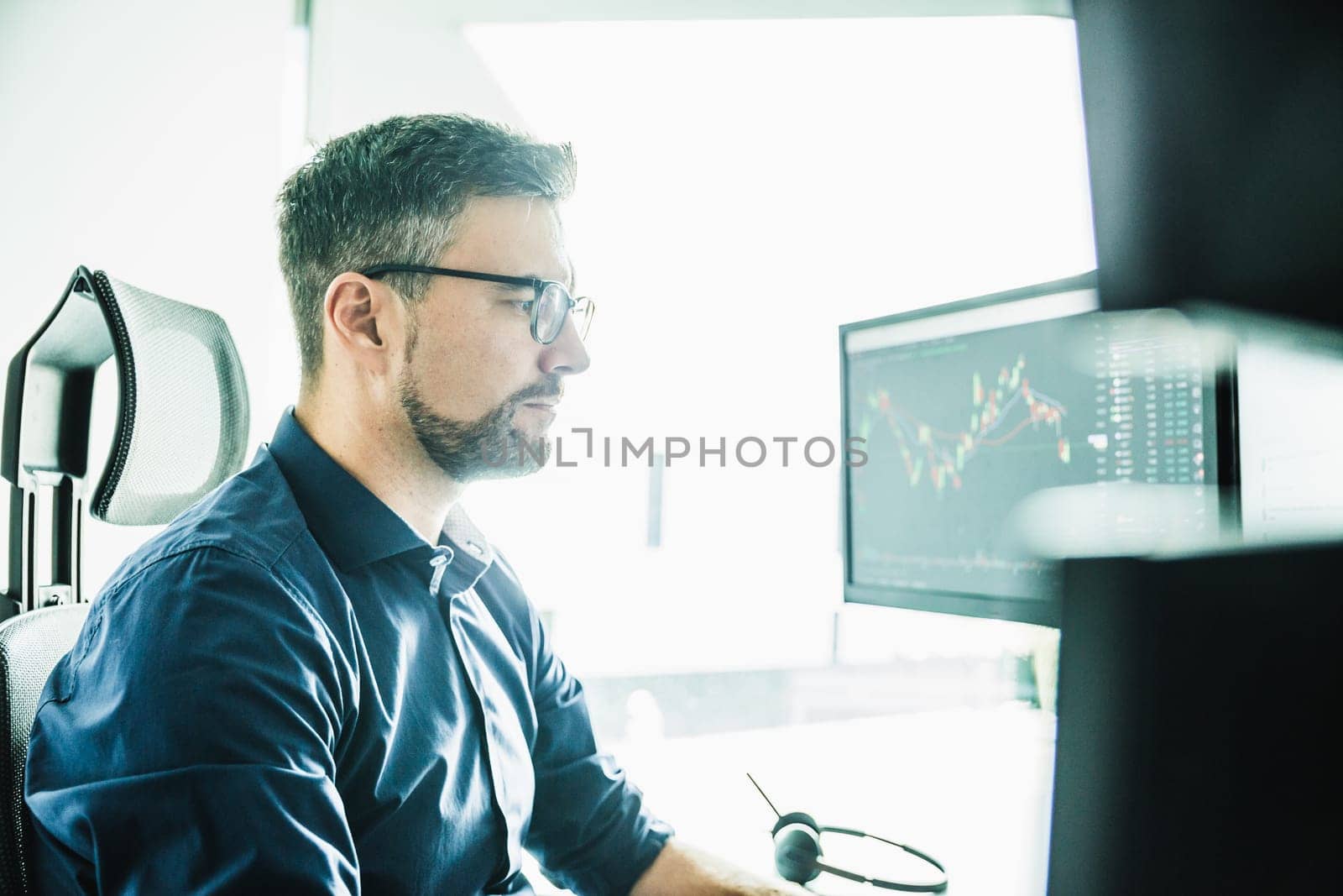 Stock broker trading online watching charts and data analyses on multiple computer screens. by kasto