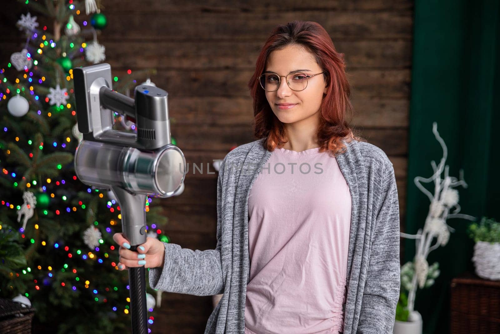 A young pretty girl is standing and holding a vacuum cleaner. At any time it is necessary to take care of tidiness and especially before any important holiday.