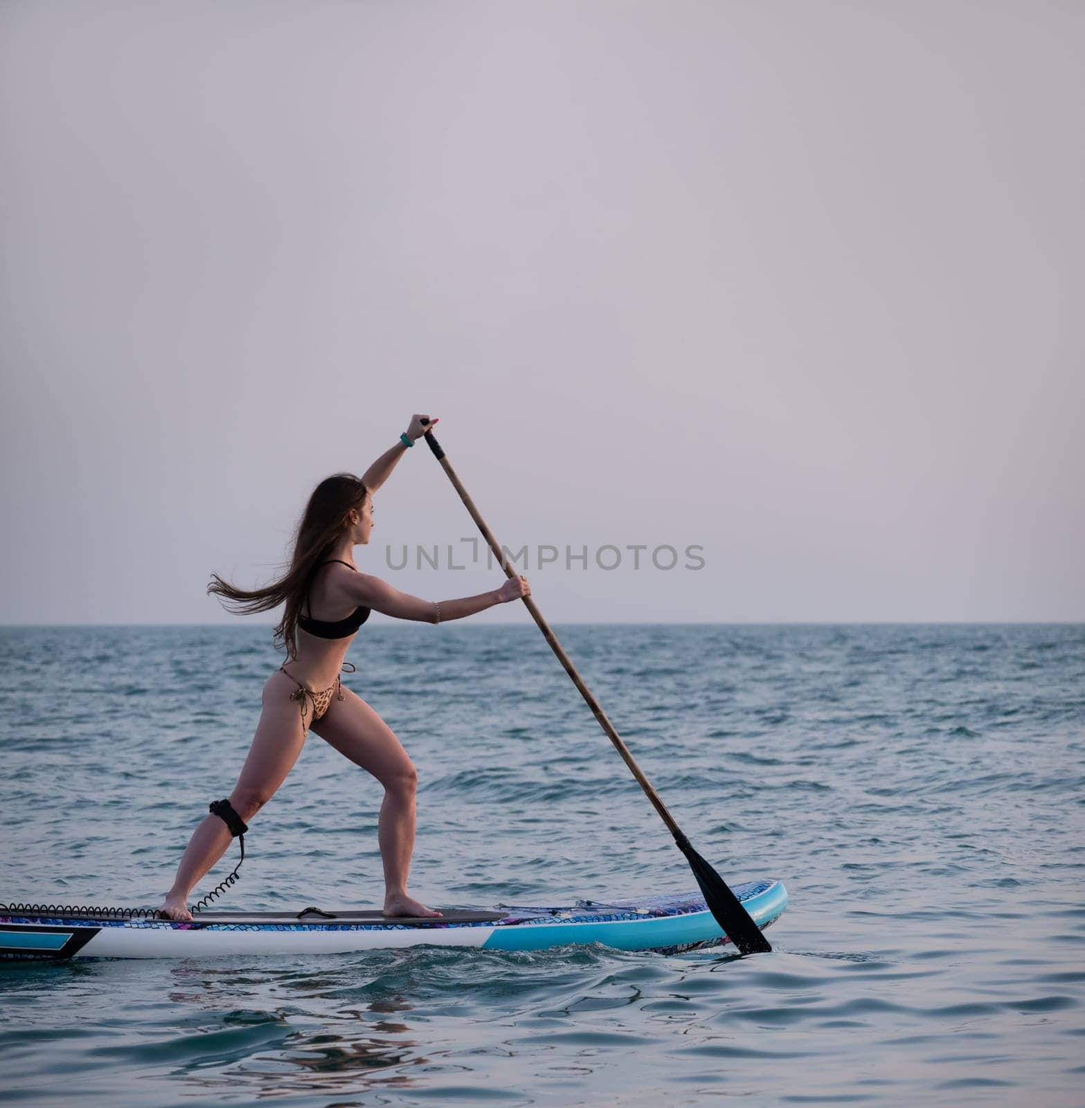 sexy girl on a sup board in the sea with a paddle professionally swims beautifully and gracefully by Rotozey