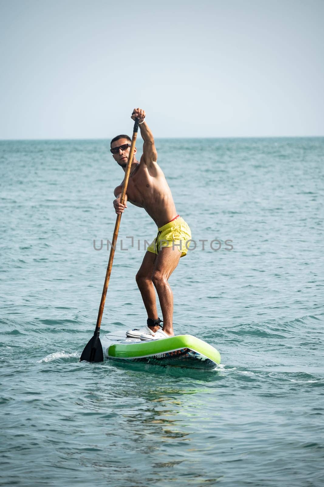 a sporty guy swims on a sup board with a paddle on the sea during the day against a beautiful sky by Rotozey