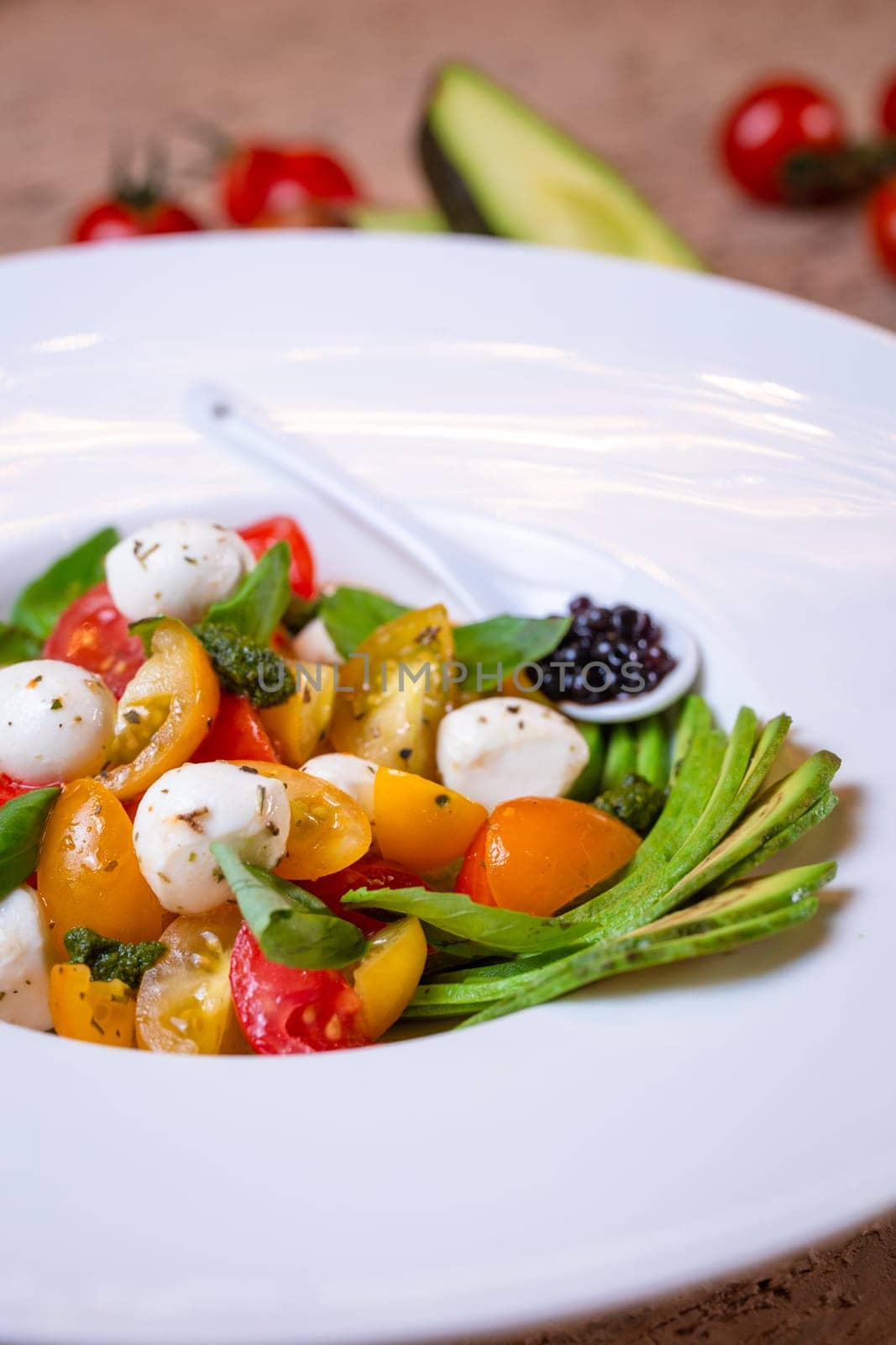 salad with avacado, mozzarella and tomatoes in a white plate by Pukhovskiy