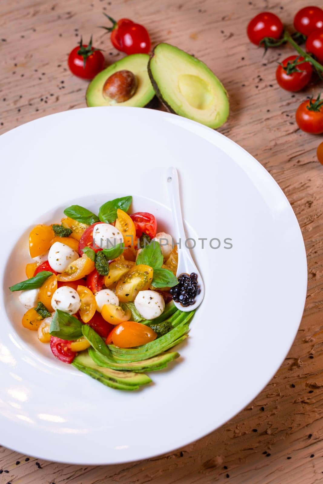 salad with avacado, mozzarella and tomatoes in a white plate by Pukhovskiy