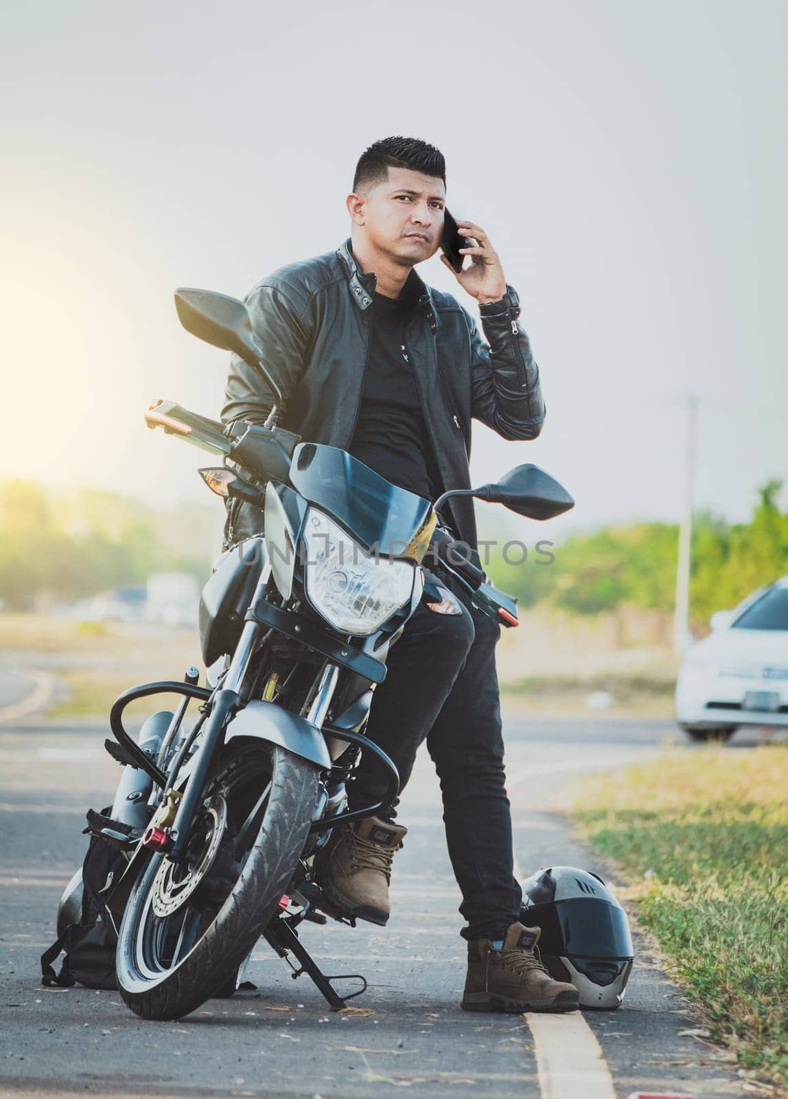 Handsome biker calling on the phone in the street. Biker sitting on motorcycle calling on the phone on the roadside. Concept of motorcyclist using the phone