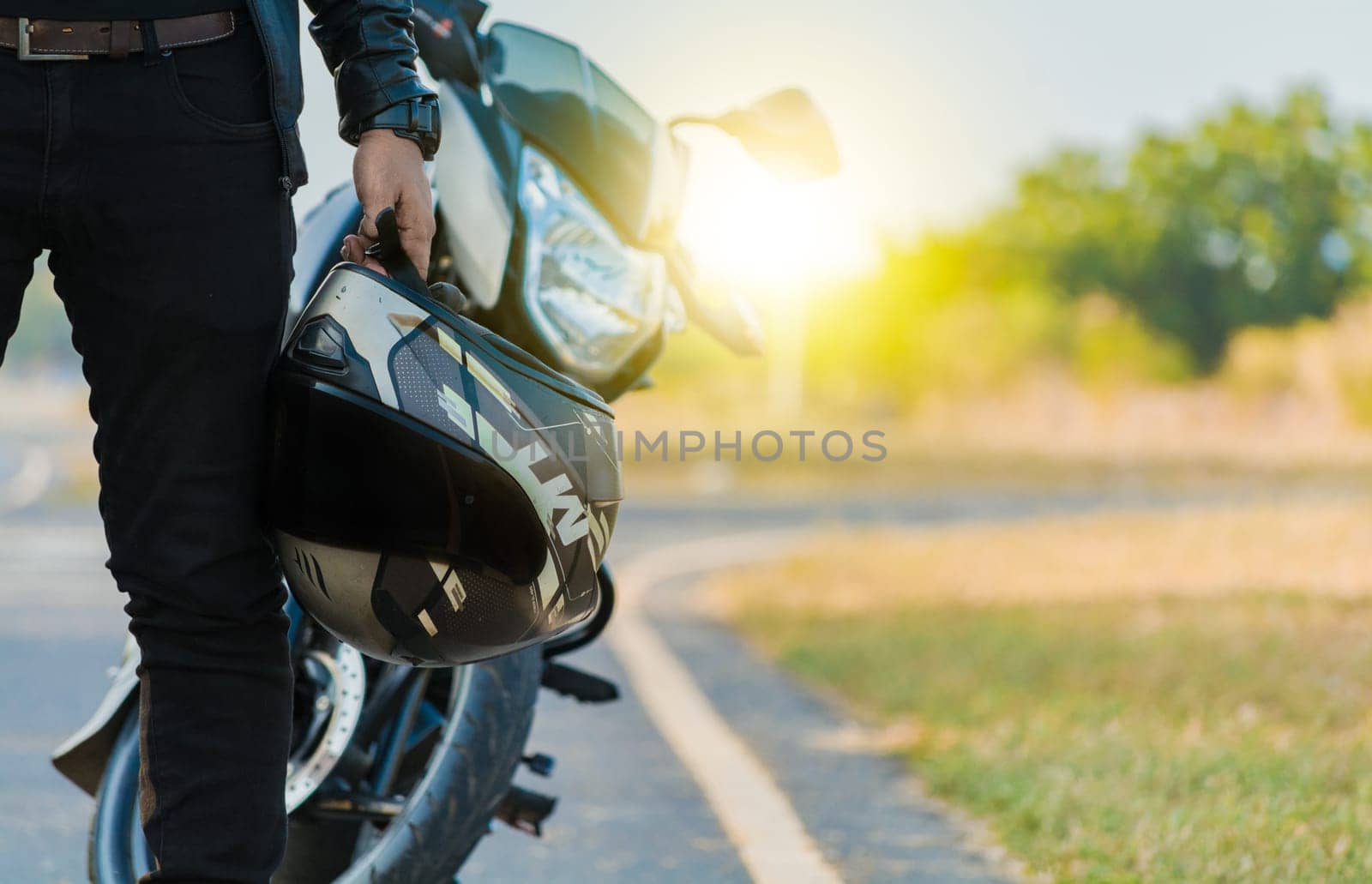 Motorcyclist holding safety helmet next to his motorbike near the road. Unrecognizable biker holding helmet next to motorbike near the road. Motorcycle safety helmet concept by isaiphoto