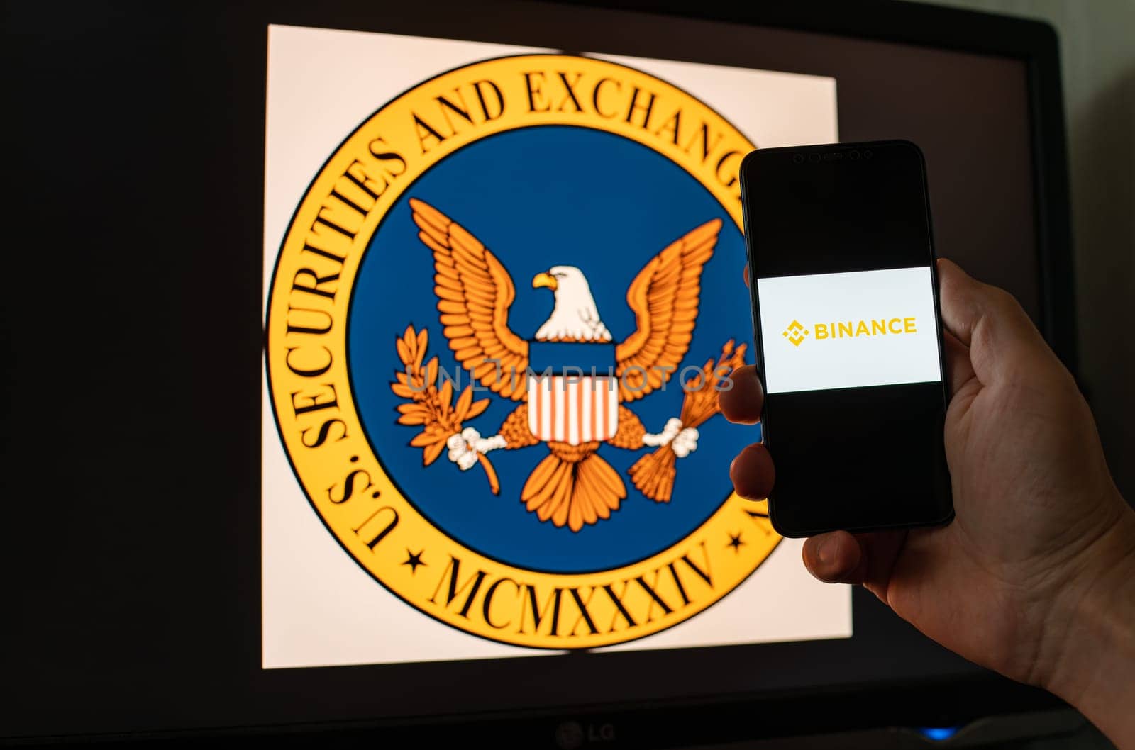 Kyiv, Ukraine - 06 June 2023: Man holds a smartphone with crypto exchange Binance on screen against the background of monitor with the SEC logo. S.E.C. sued on Binance through money laundering in BNB