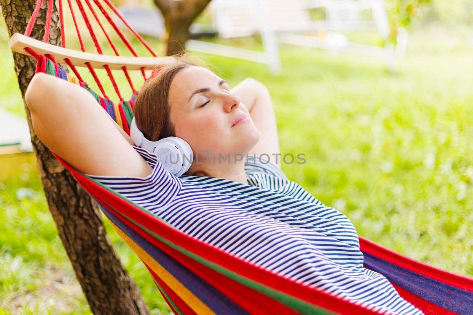 Young woman in headphones listening to music while resting in hammock outdoors.