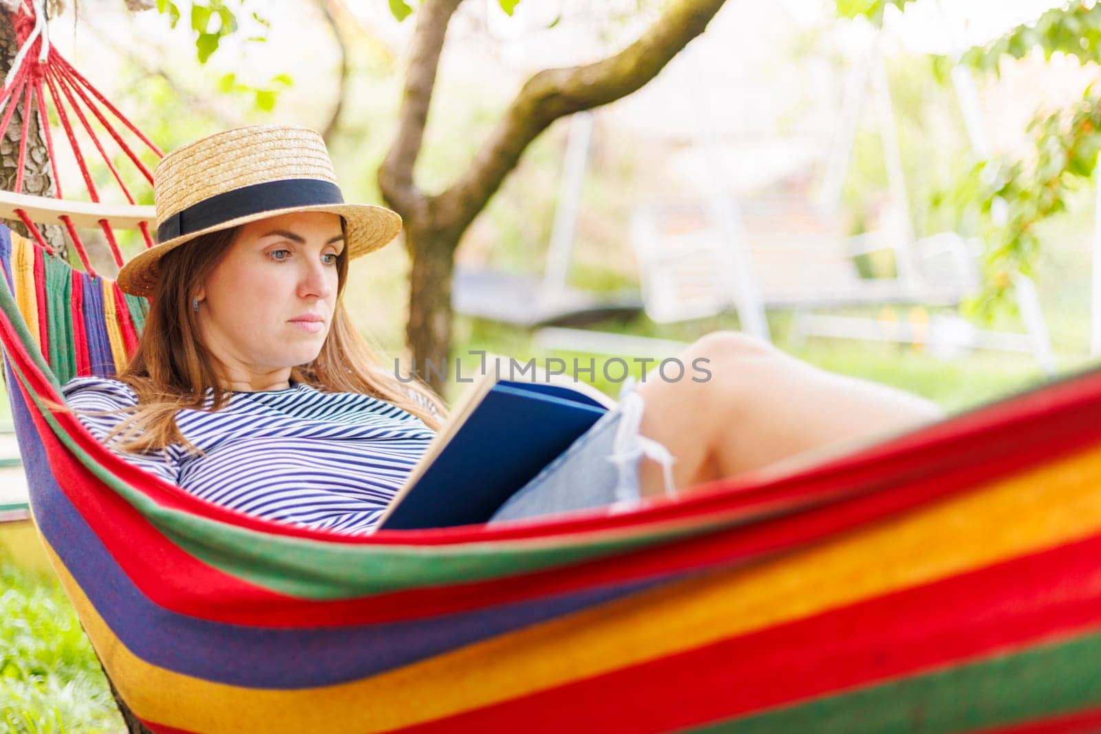 Young woman reading book while lying in comfortable hammock at green garden by andreyz