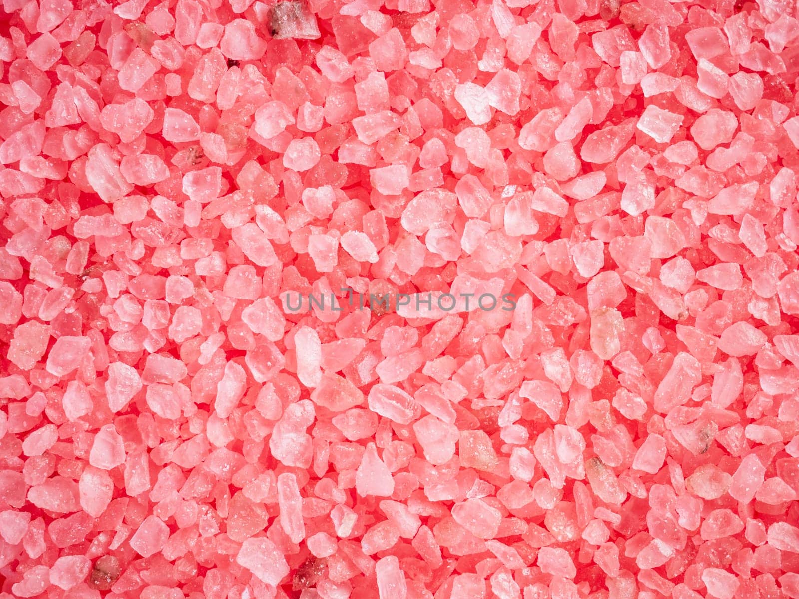 Beauty and body care concept. Pink colored salt crystals as a background. Aromatic roseate bath salt with litchi and patchouli scent. Large sprinkled crystals of crimson sea salt. Close up.